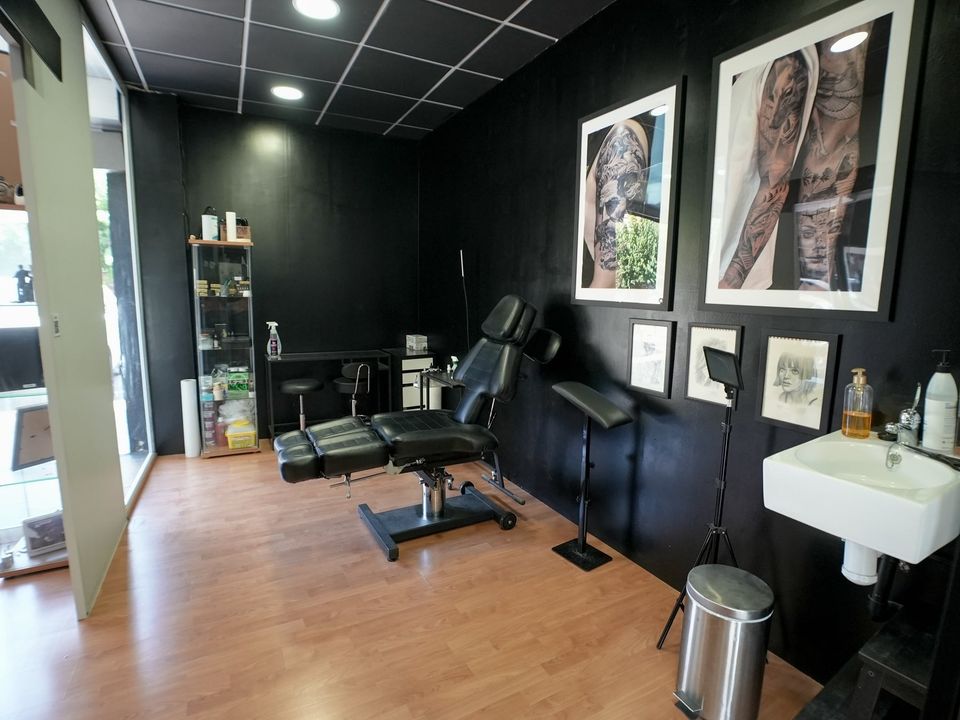 Cabina de tatuaje con camilla negra, lavamanos y fotos enmarcadas de tatuajes realistas en la pared