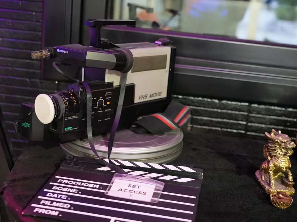 Cámara de vídeo VHS antigua sobre una lata de película, con una claqueta de cine y una acreditación «Set access»