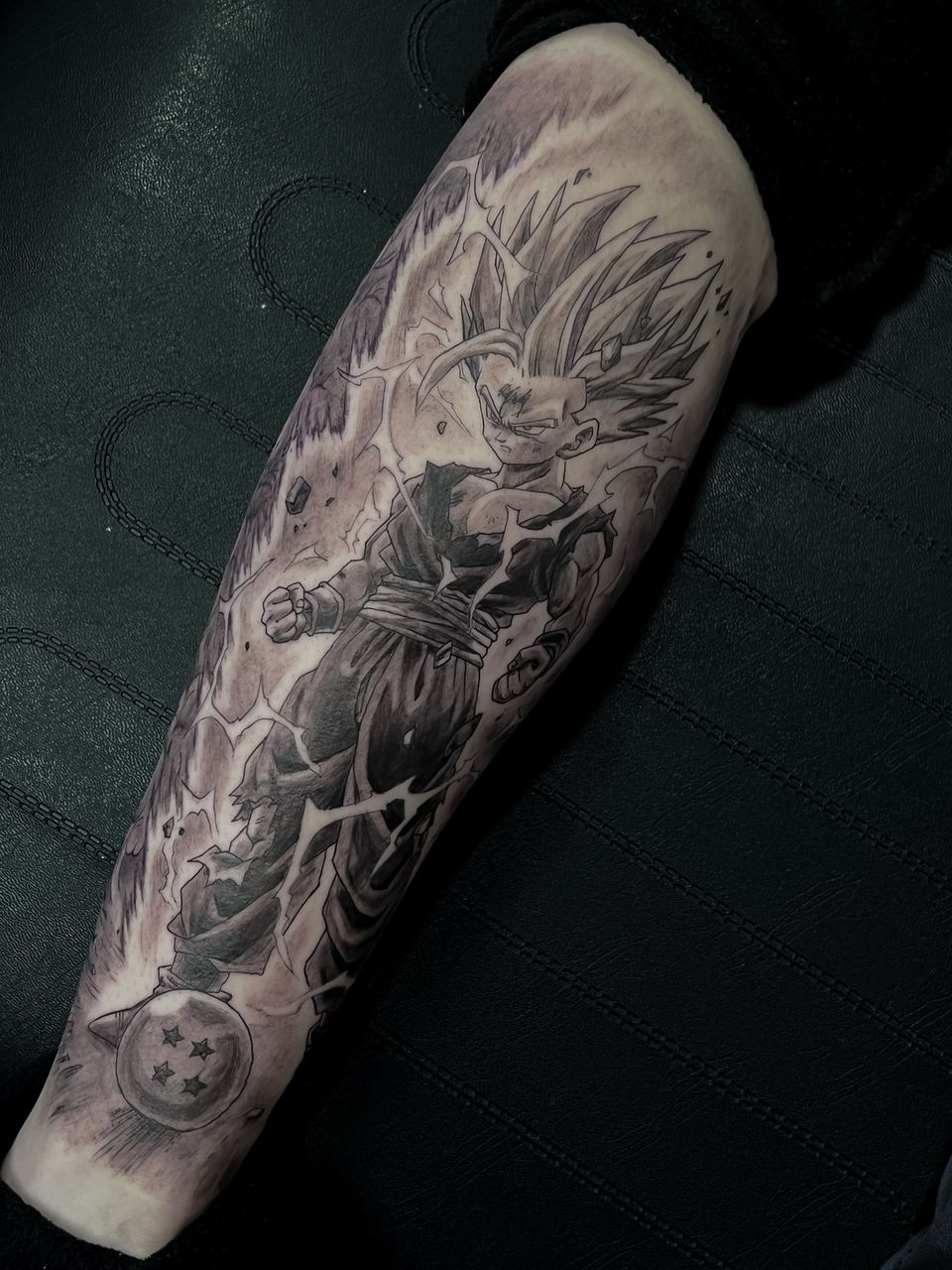 Tatuaje de anime en el gemelo, en negro y grises: Gohan Super Saiyan de Dragon Ball rodeado de rayos, con una bola de dragón