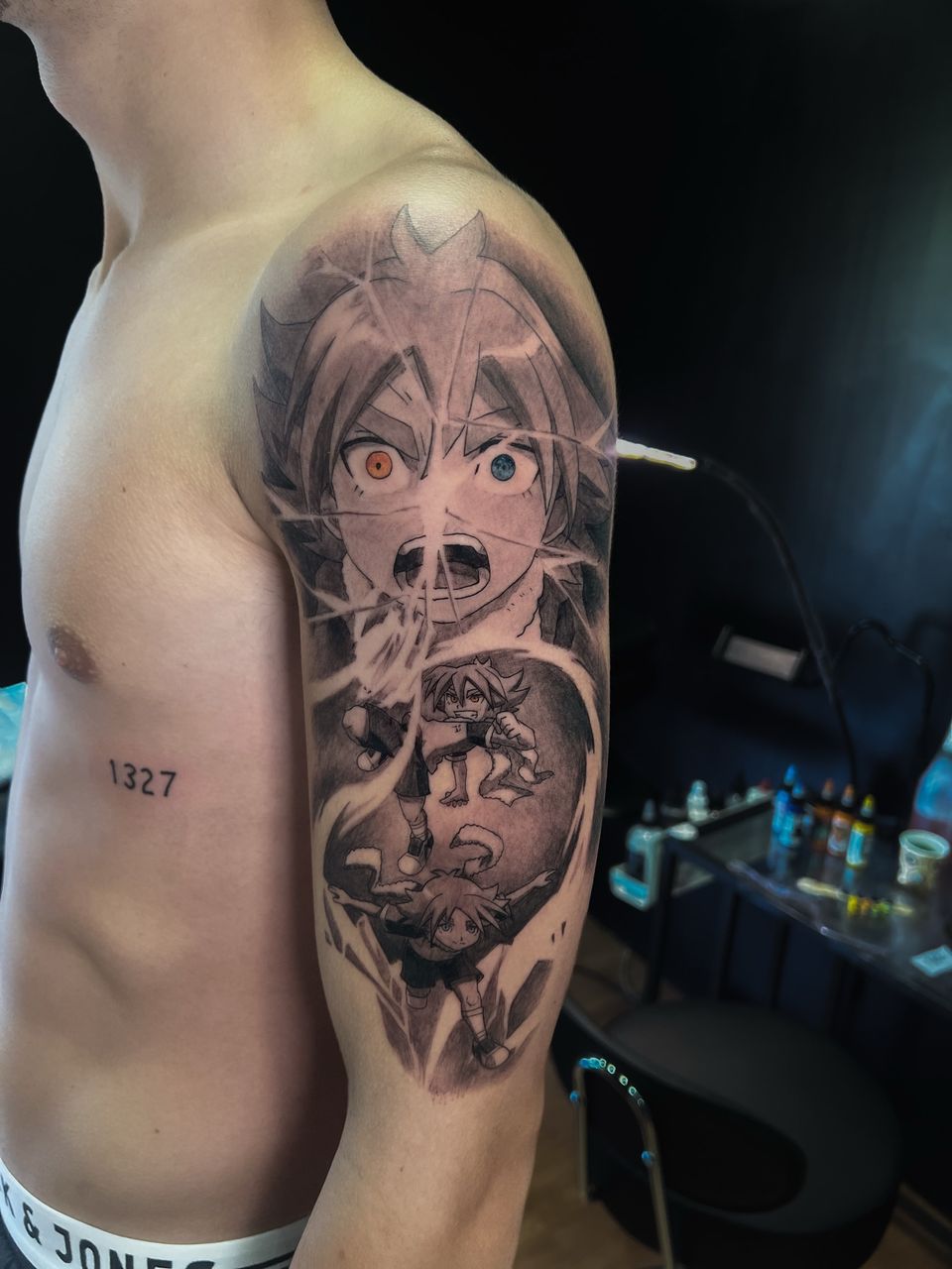 Tatuaje de anime de Inazuma Eleven en el brazo y el hombro: rostro de personaje con un ojo naranja y otro azul sobre dos escenas de la serie, en negro y grises