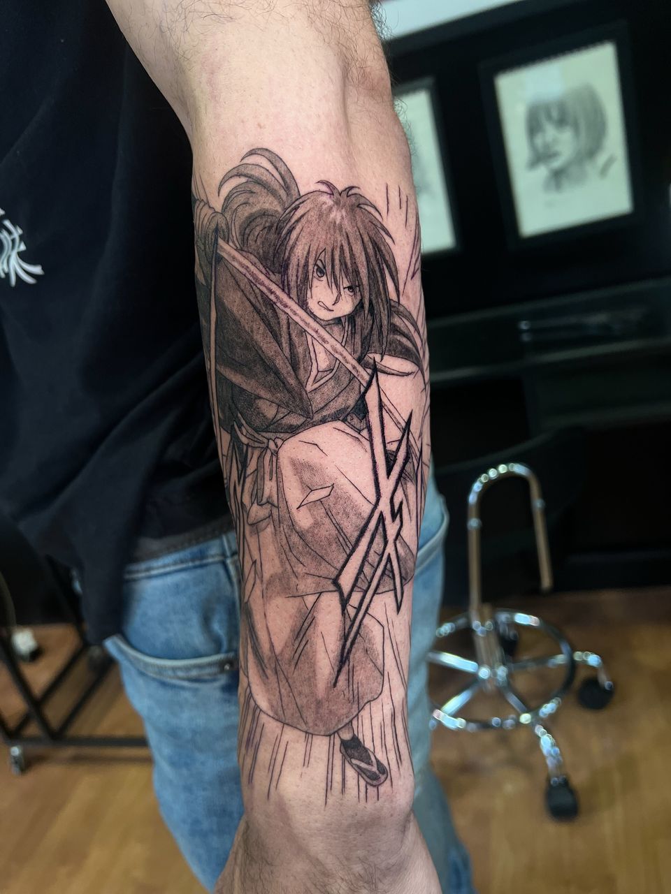 Tatuaje de anime estilo manga en el antebrazo: Kenshin Himura de Rurouni Kenshin con su espada, en negro y grises