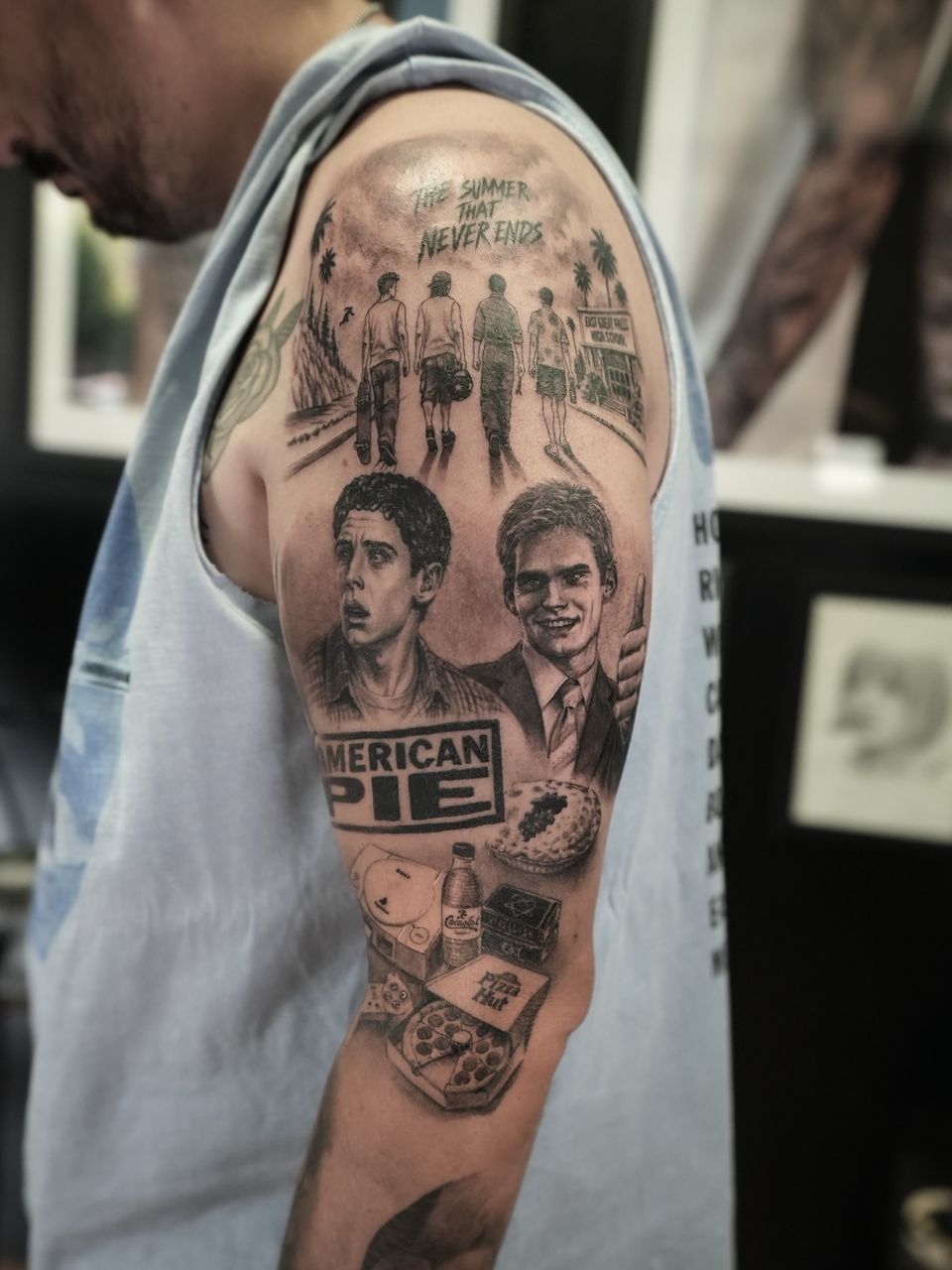 Tatuaje realista en el hombro y el brazo inspirado en American Pie: retratos de los personajes, cuatro amigos caminando, una pizza y una consola, en negro y grises