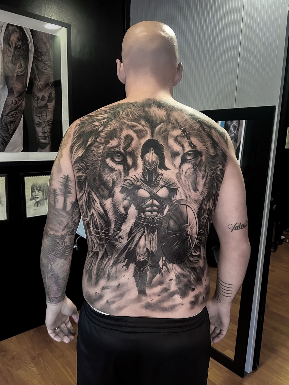 Espalda completa realista: guerrero espartano con escudo delante del rostro de un león, en negro y grises