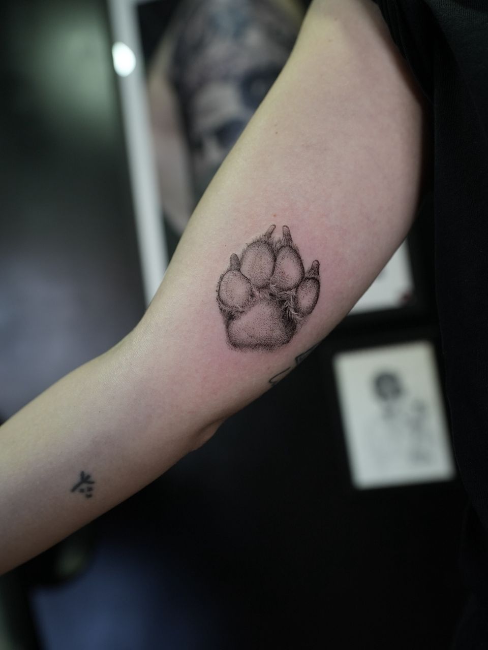 Tatuaje realista en la cara interna del brazo: huella de perro con pelo, sombreada con puntos, en negro y grises