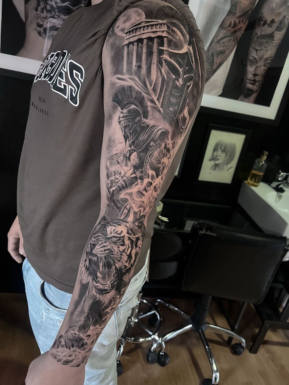Manga completa realista en el brazo: guerrero espartano, templo griego, casco y un tigre rugiendo, en negro y grises