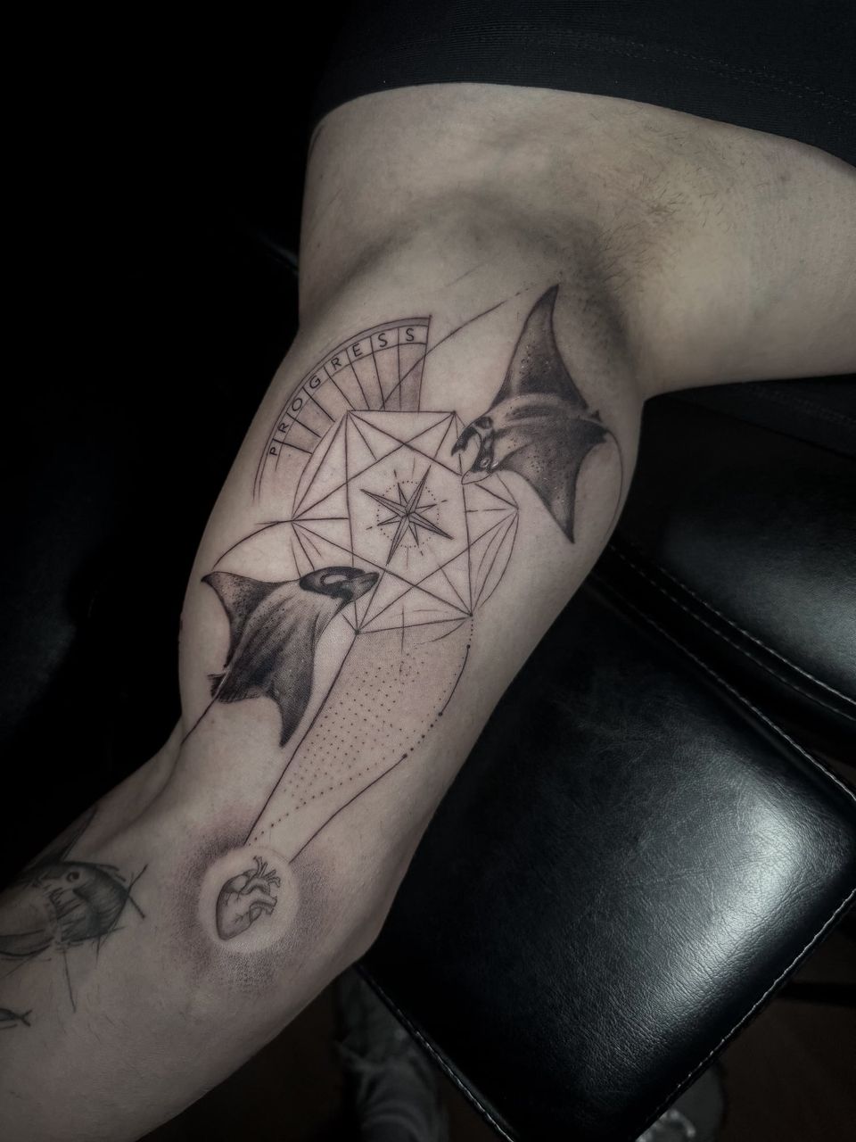 Tatuaje conceptual en la cara interna del brazo: dos mantarrayas alrededor de un poliedro con una rosa de los vientos, la palabra «Progress» y un corazón anatómico, con sombreado de puntos