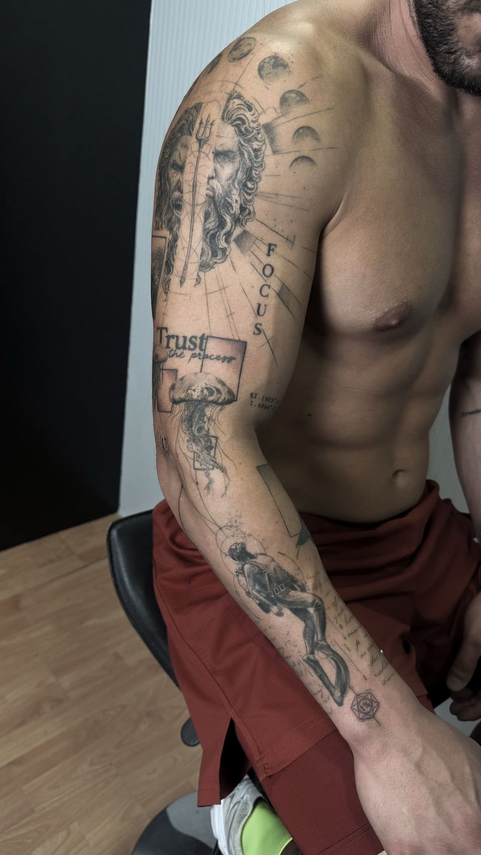 Manga completa conceptual en el brazo: Poseidón con doble rostro y tridente, fases de la luna, una medusa, un buzo, las palabras «Focus» y «Trust the process», coordenadas y textos manuscritos, en negro y grises