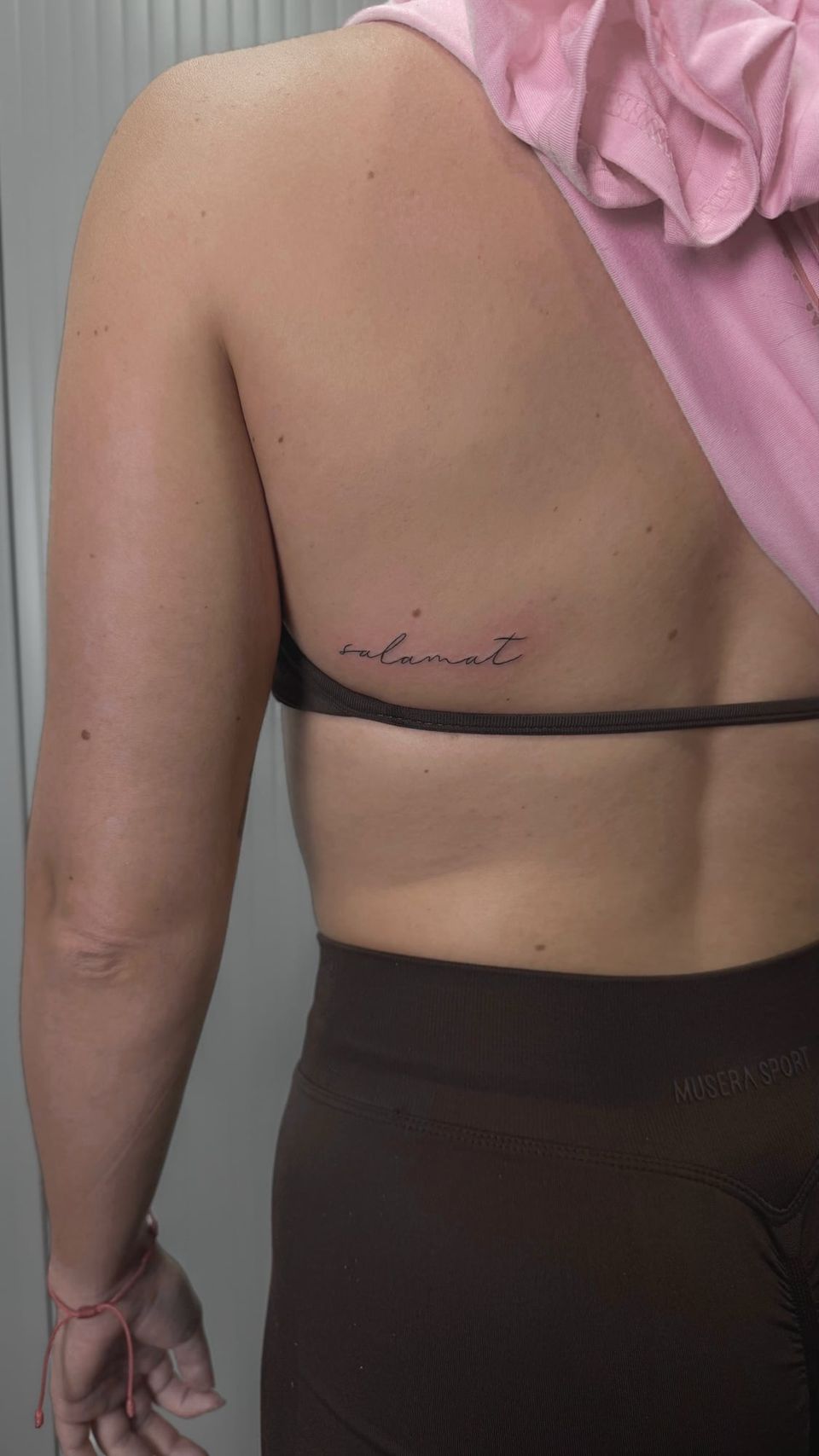 Tatuaje de línea fina en la espalda: la palabra «salamat» en letra manuscrita